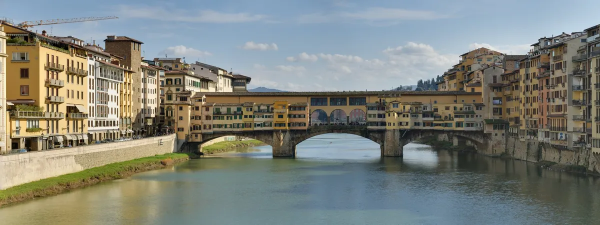 A panoramic view of the Ponte Vecchio bridge over the Arno River, with its shops and apartments built along the span