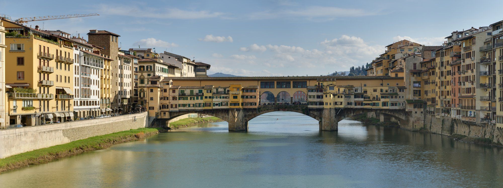 A panoramic view of the Ponte Vecchio bridge over the Arno River, with its shops and apartments built along the span
