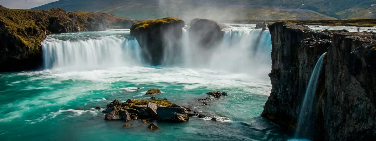 Goðafoss's horseshoe-shaped curtain of falls pouring into a turquoise pool below moss-topped rock pillars