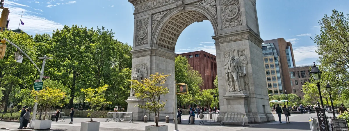 The Washington Square Arch on a sunny day, with trees and pedestrians in Washington Square Park around it