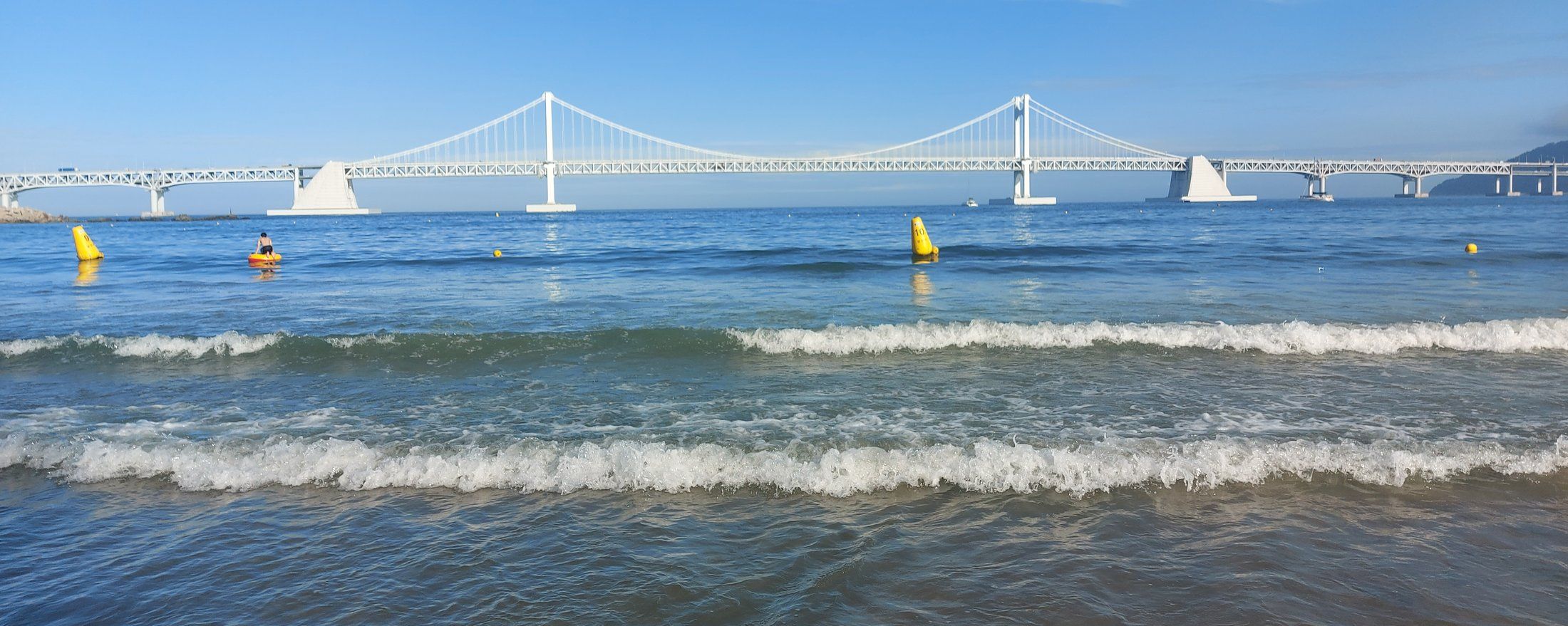 Waves rolling onto Gwangalli Beach with the white suspension towers of Gwangan Bridge spanning the bay behind