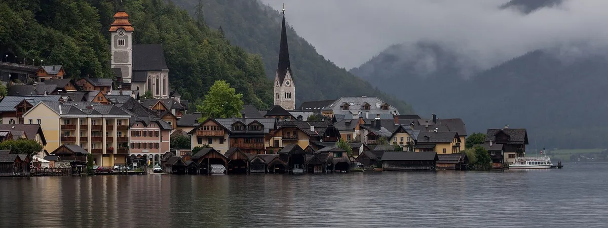 Hallstatt's lakeside houses and twin church towers reflected in Lake Hallstatt, backed by forested mountains