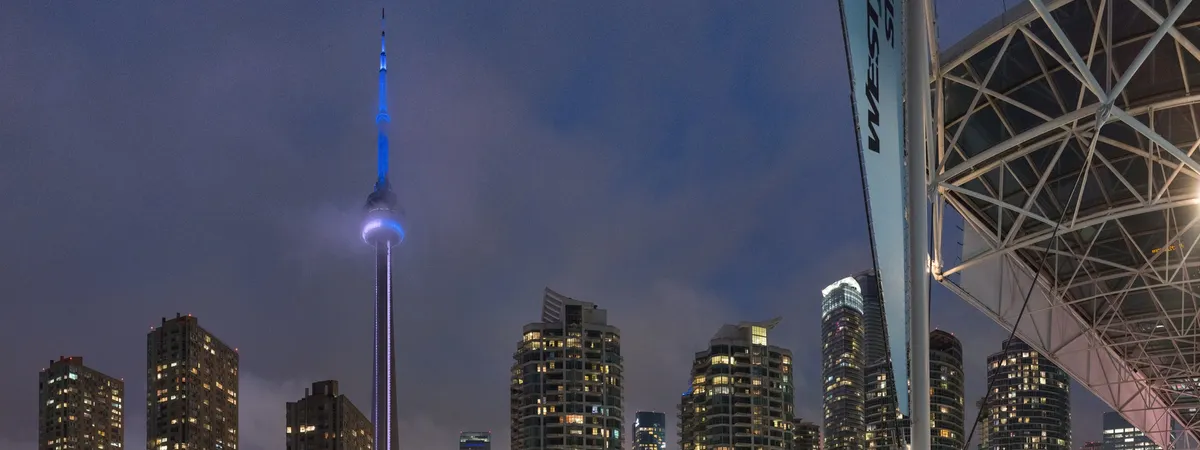 The CN Tower lit blue at dusk above the Harbourfront Centre stage and downtown condo towers, seen from Toronto's waterfront