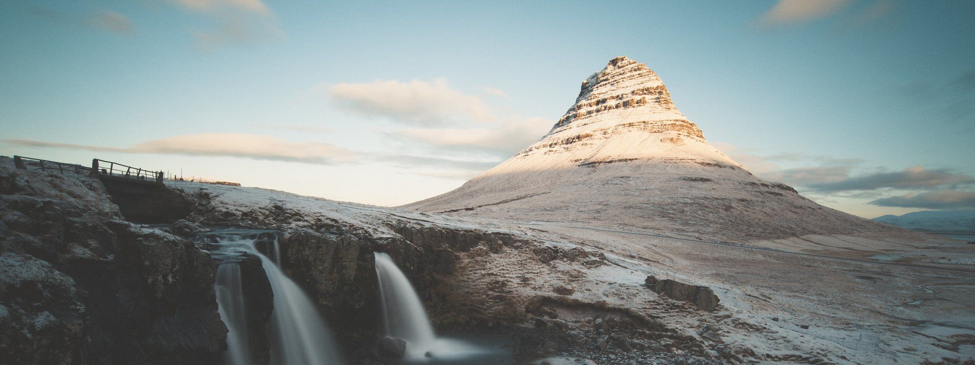 Kirkjufell mountain and Kirkjufellsfoss waterfall at sunrise on Iceland's Snæfellsnes Peninsula, dusted with snow