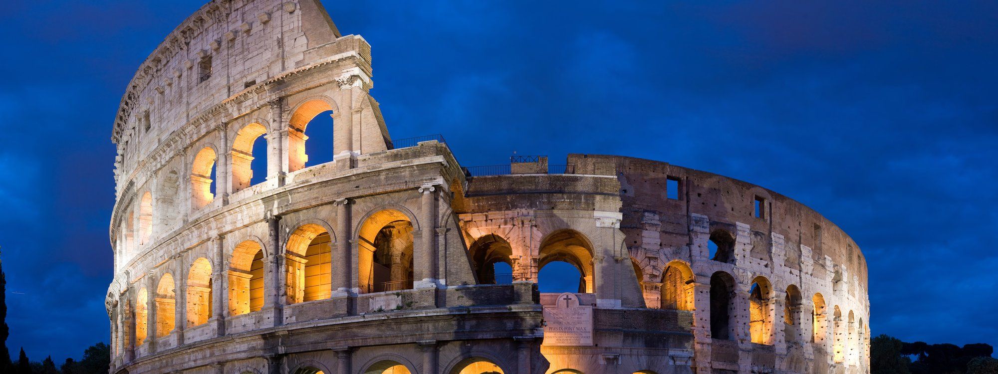 The Colosseum in Rome lit up at dusk against a deep blue evening sky