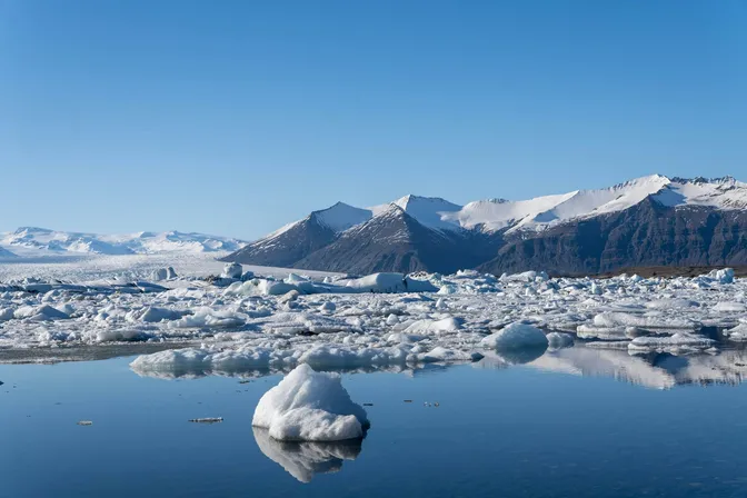 White icebergs drifting on Jökulsárlón's still water, snow-capped mountains reflected behind them