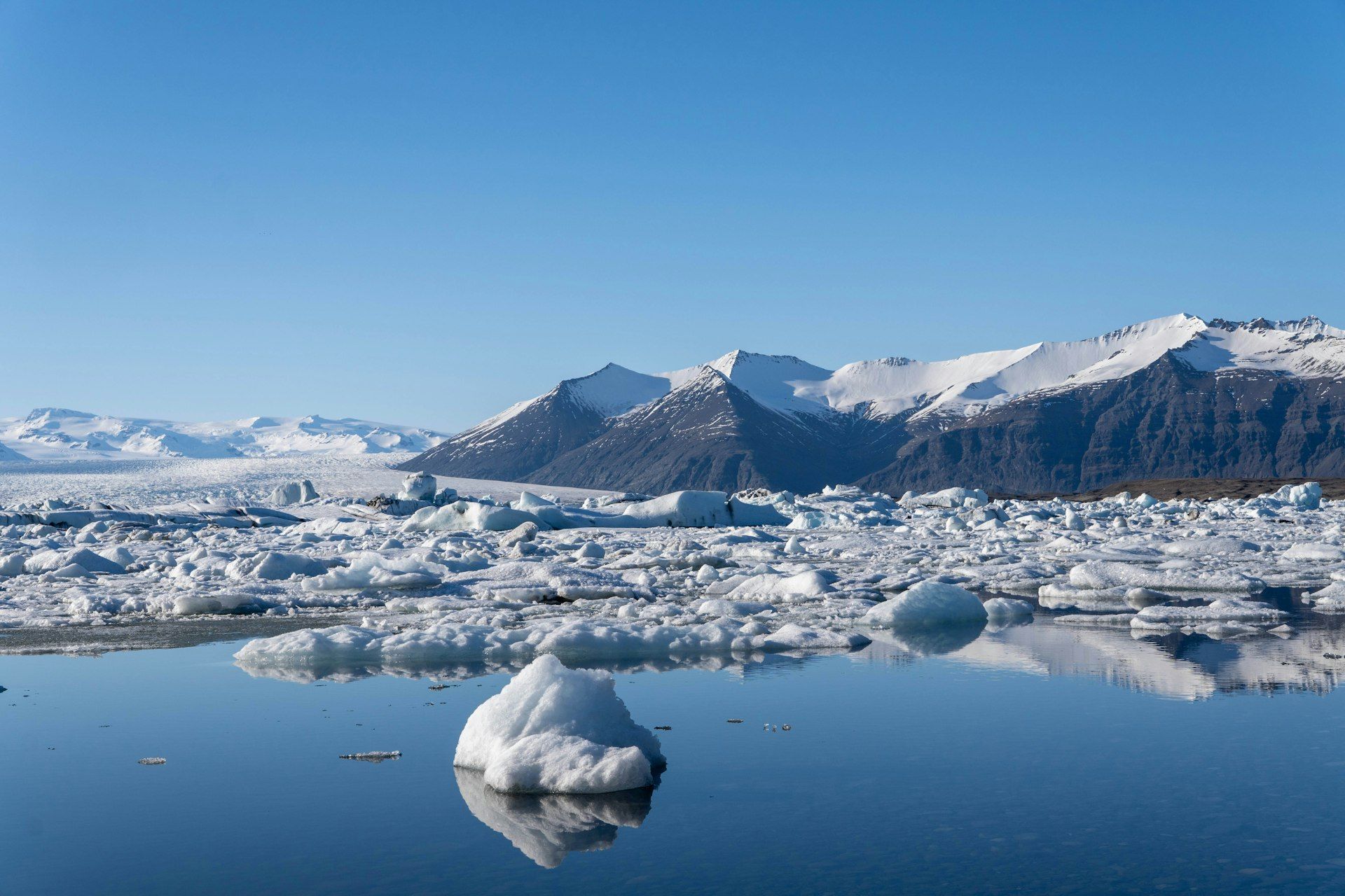 White icebergs drifting on Jökulsárlón's still water, snow-capped mountains reflected behind them