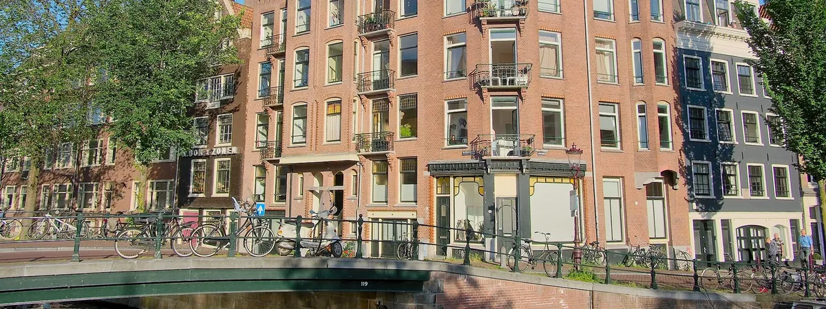 A canal-side bridge lined with parked bicycles in front of gabled brick houses in the Jordaan