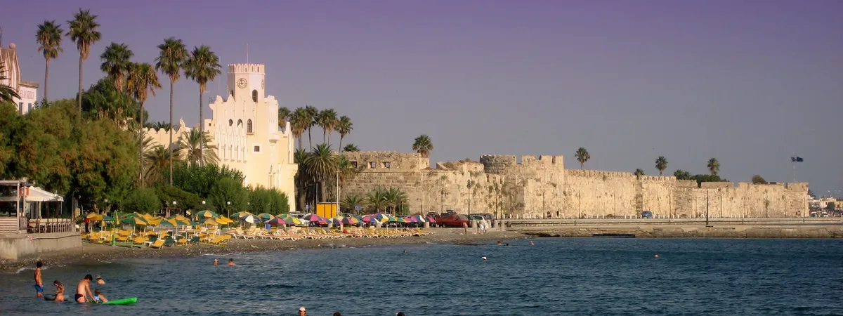 Las murallas medievales del castillo de Neratzia custodiando el puerto de Kos, con palmeras y una playa delante