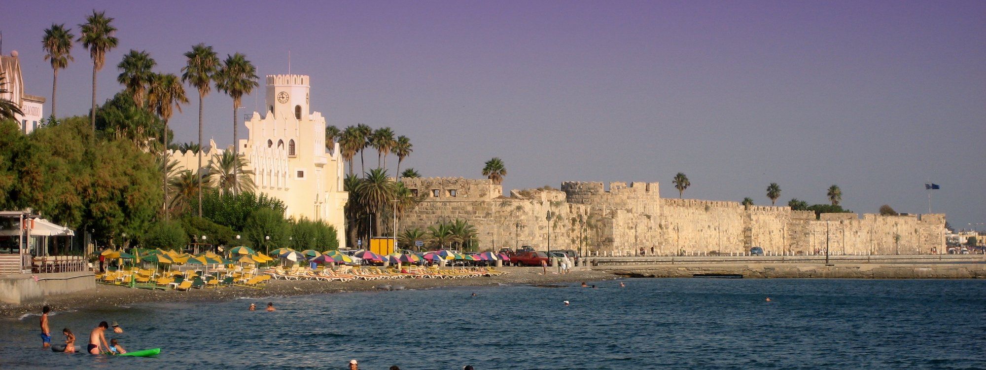 Las murallas medievales del castillo de Neratzia custodiando el puerto de Kos, con palmeras y una playa delante