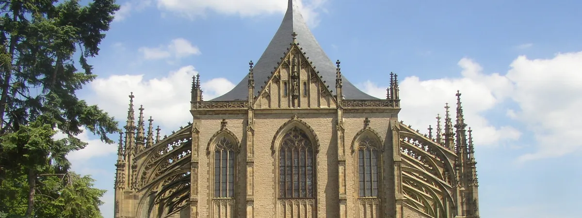 St. Barbara's Cathedral in Kutná Hora seen from the approach path along Barborská Street, its Gothic spires and flying buttresses rising above the valley