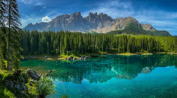 The green water of Lago di Carezza reflecting pine forest and the Latemar range