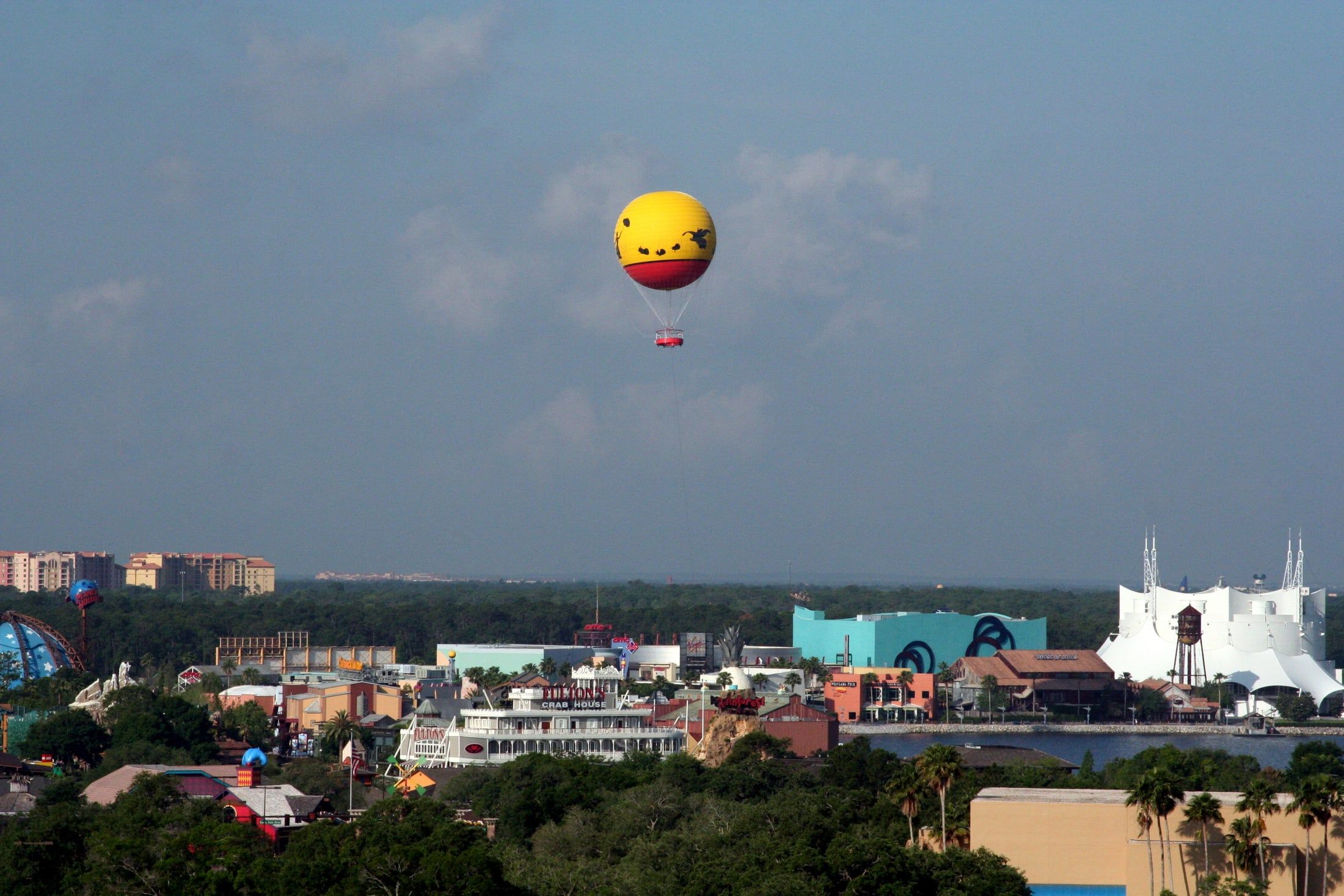 The yellow Characters in Flight tethered balloon rising over the shops and waterfront of Disney Springs