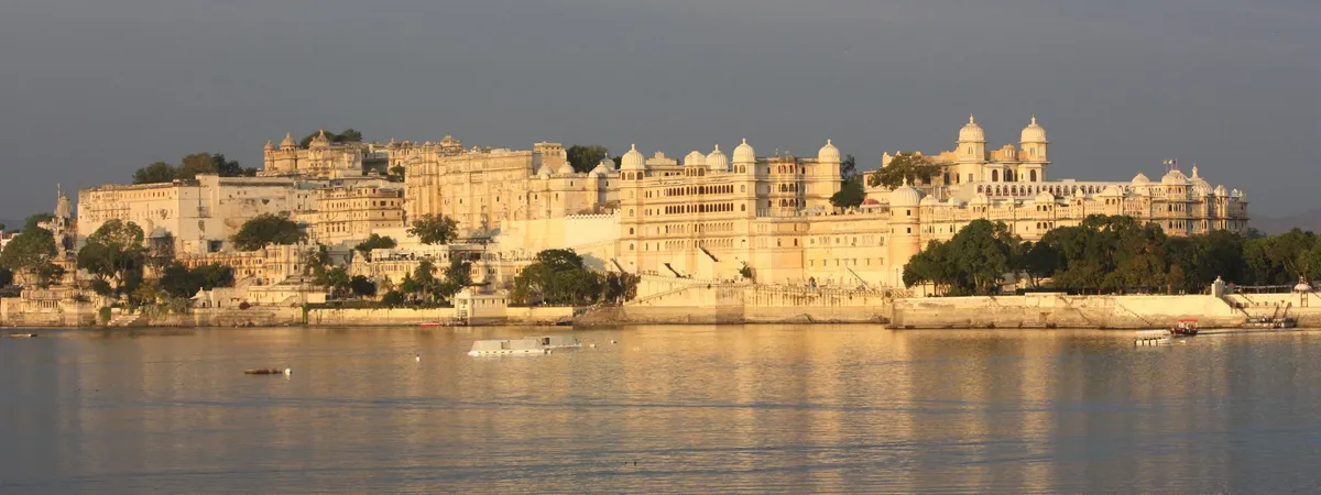 Udaipur's City Palace glowing gold at sunset above Lake Pichola, seen from a boat on the water