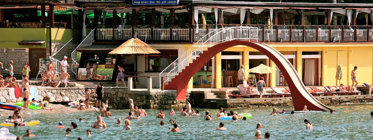 Sunbathers and swimmers at Lapad Beach in Dubrovnik with a beachfront café behind them