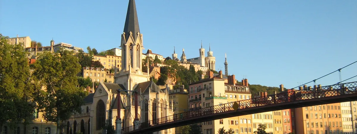 The Saône river in Lyon at sunset, with the church of Saint-Georges, colorful old-town buildings, and Notre-Dame de Fourvière Basilica visible on the hill above