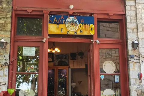 בית אבן מסורתי עם מרפסות עץ אדומות וחנות קרמיקה הנפתחת לרחוב הראשי המרוצף של מקריניצה