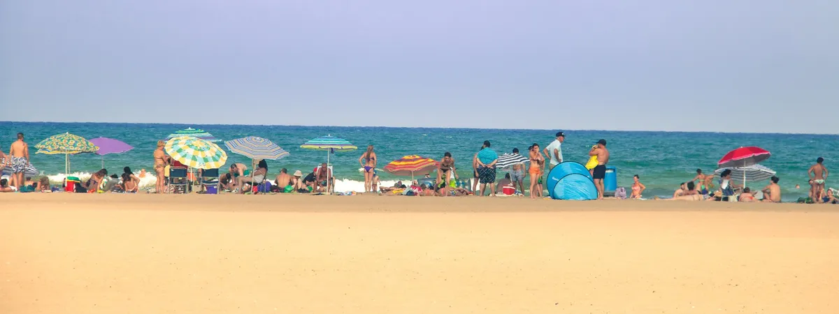 Beachgoers and striped umbrellas on the sand at Malvarrosa Beach in Valencia