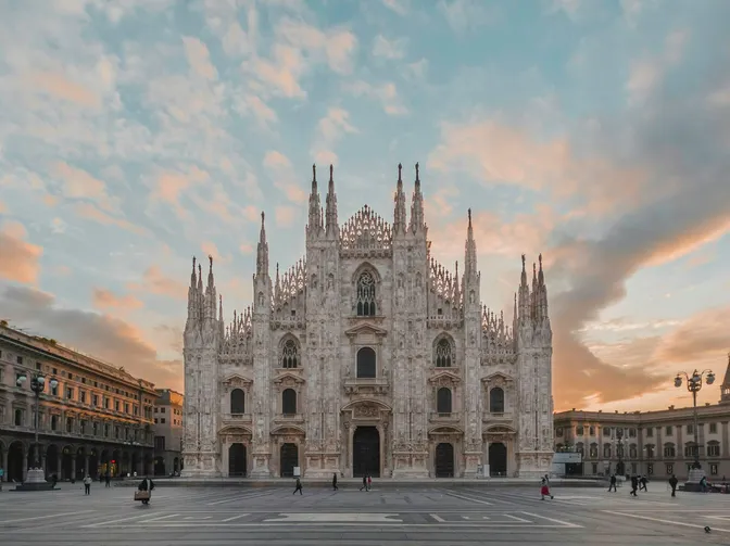 The marble facade and spires of the Duomo di Milano at dusk, seen across an almost empty Piazza del Duomo