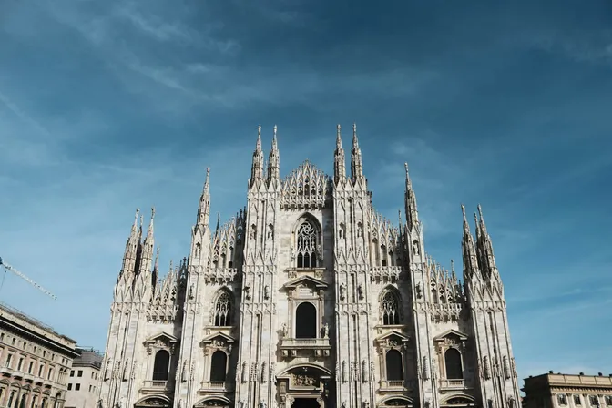 The white marble west front of the Duomo di Milano, its spires and pinnacles against a clear sky