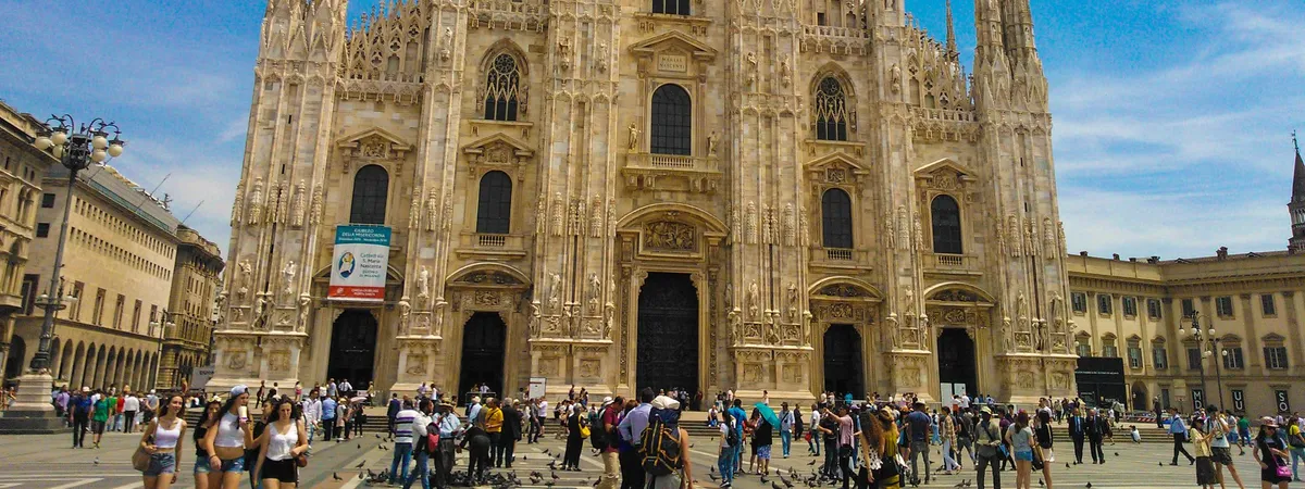 The white marble Gothic facade of Milan Cathedral (the Duomo), with its spires and statues, seen from Piazza del Duomo