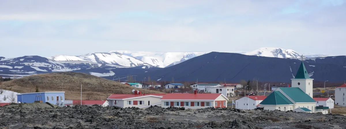 Reykjahlíð village on the shore of Lake Mývatn, with the green-roofed church, low houses, and snow-capped mountains behind