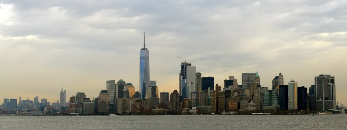Lower Manhattan skyline seen across the Hudson River at dusk, with One World Trade Center rising above the surrounding towers
