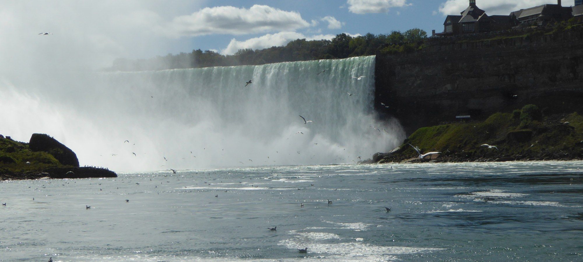 Horseshoe Falls seen from the Canadian side, with mist rising off the water and Table Rock's building on the clifftop above