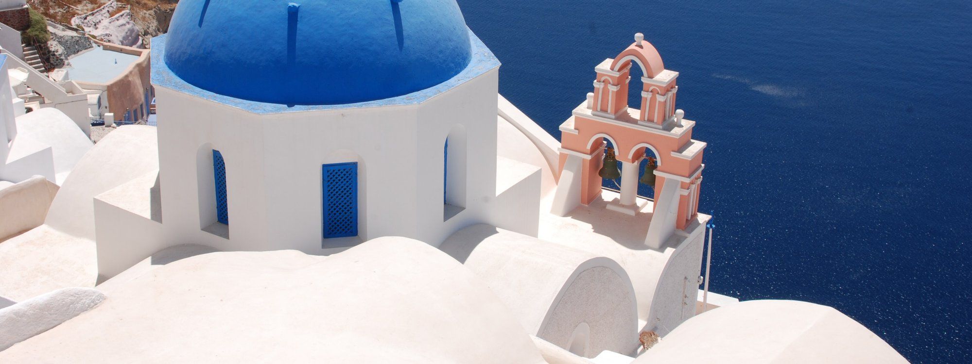 A blue-domed church with a coral-pink bell tower overlooking the caldera in Oia, Santorini