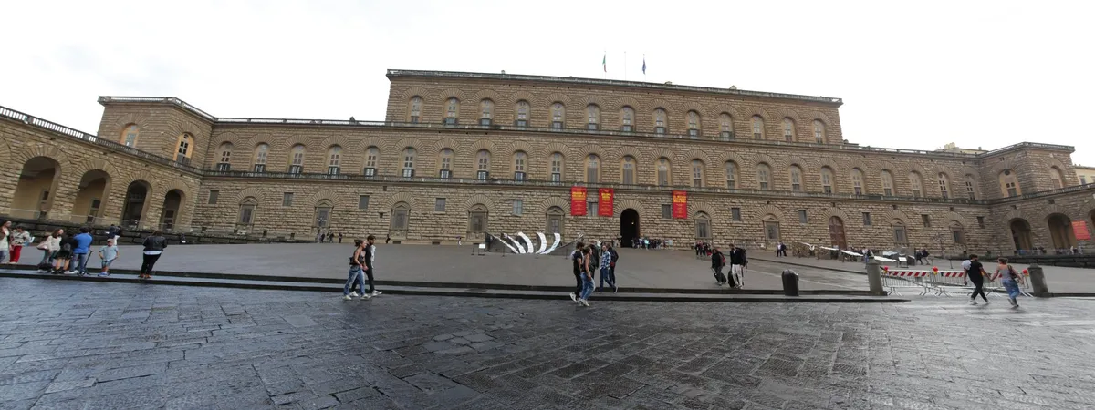 The long rusticated stone facade of Palazzo Pitti in Florence's Oltrarno district, with its courtyard piazza in front