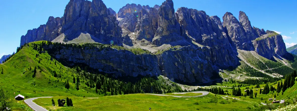 The Passo Gardena road looping through green summer meadows below the Dolomite walls of the Sella group