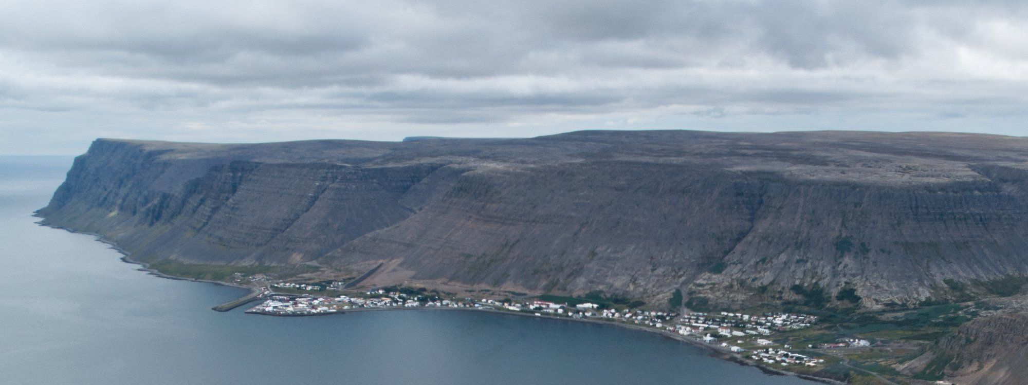 Patreksfjörður strung along the shoreline of its fjord beneath a long flat-topped cliff wall