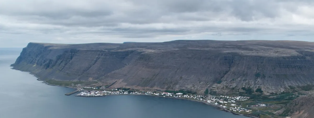 Patreksfjörður strung along the shoreline of its fjord beneath a long flat-topped cliff wall