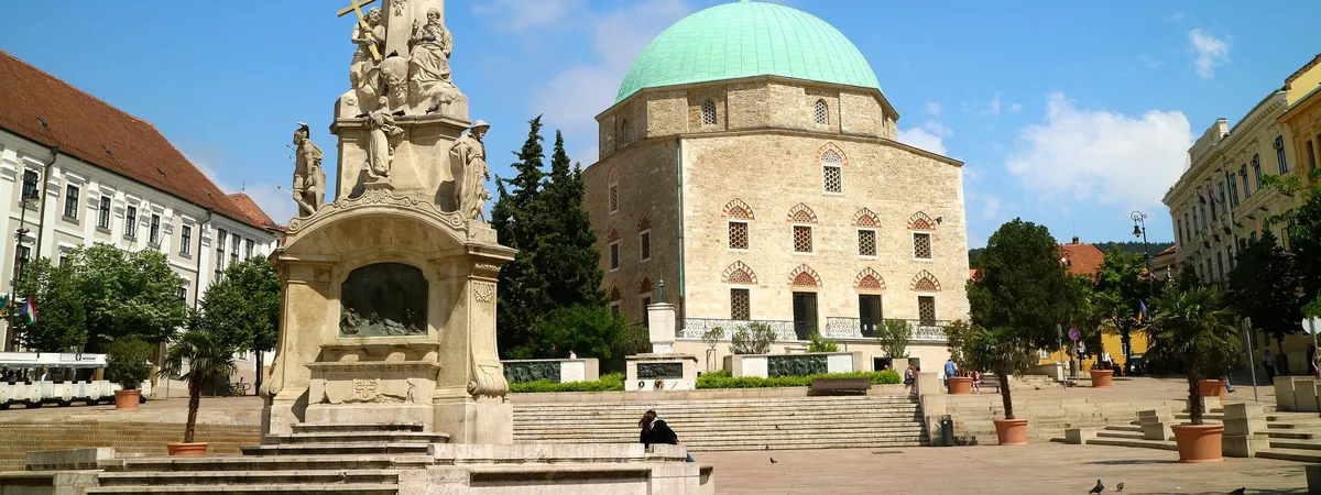 The green-domed Mosque of Pasha Qasim and the Holy Trinity column on Széchenyi tér in Pécs under a clear blue sky