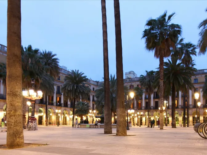 La Plaça Reial al anochecer, con sus palmeras y farolas diseñadas por Gaudí iluminando la plaza porticada