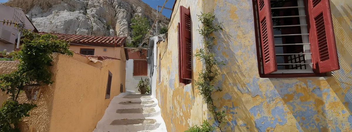 A narrow whitewashed alley with red shutters and terracotta roofs in Anafiotika, Plaka's Cycladic-style quarter beneath the Acropolis rock