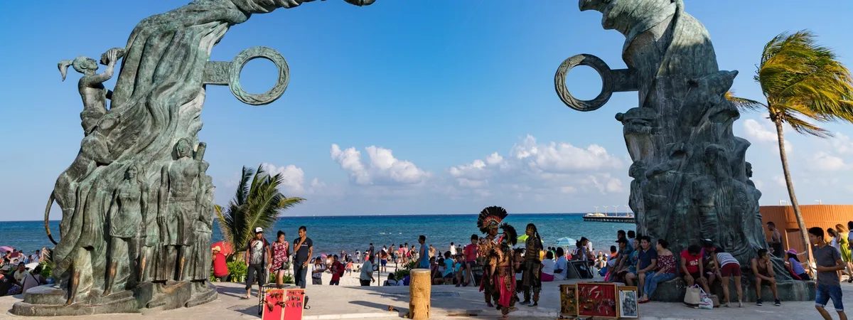 The bronze Portal Maya archway sculpture at Parque Los Fundadores in Playa del Carmen, framing the beach and Caribbean Sea behind it