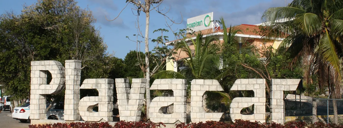 אותיות אבן שמאייתות 'Playacar' בכניסה הראשית לקהילה, מוקפות בעצי דקל ונוף טרופי