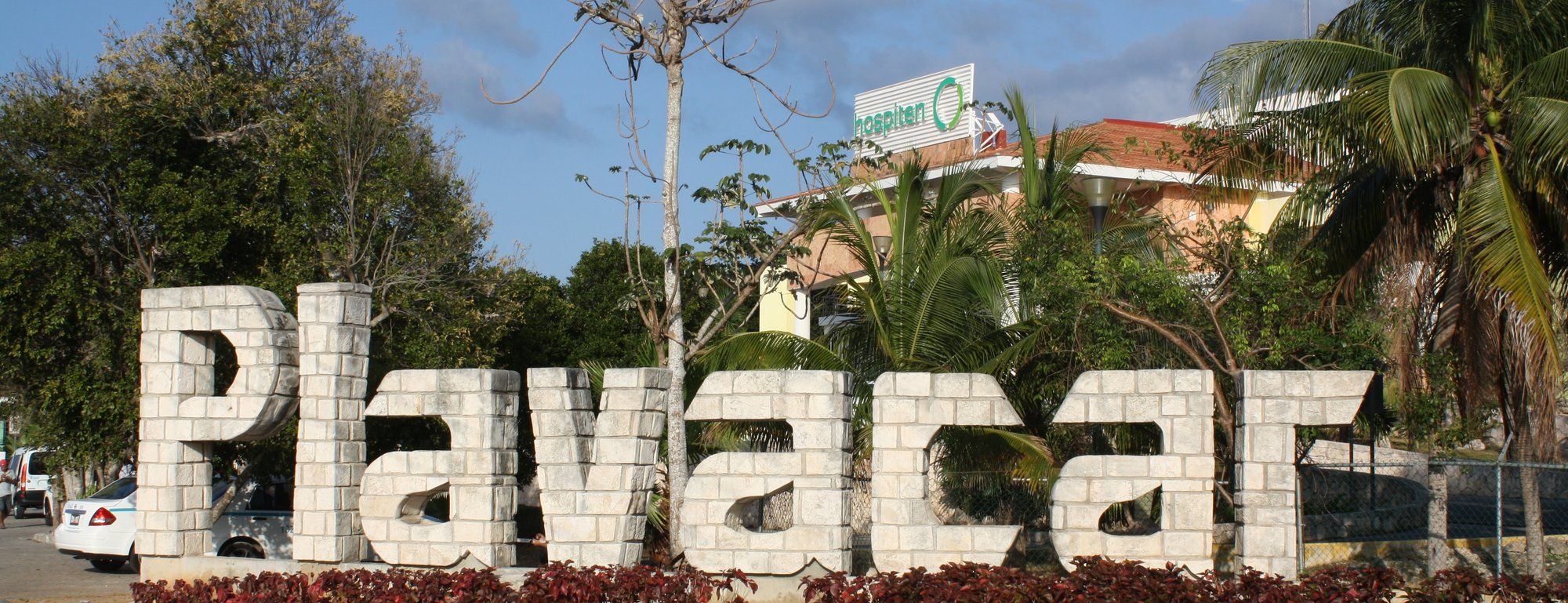 Stone letters spelling Playacar at the community's main entrance, surrounded by palm trees and tropical landscaping