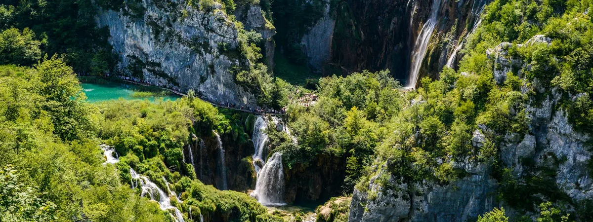 Plitvice's Lower Lakes from above: turquoise pools and cascades in a forested limestone canyon, with the tall Veliki slap waterfall on the right