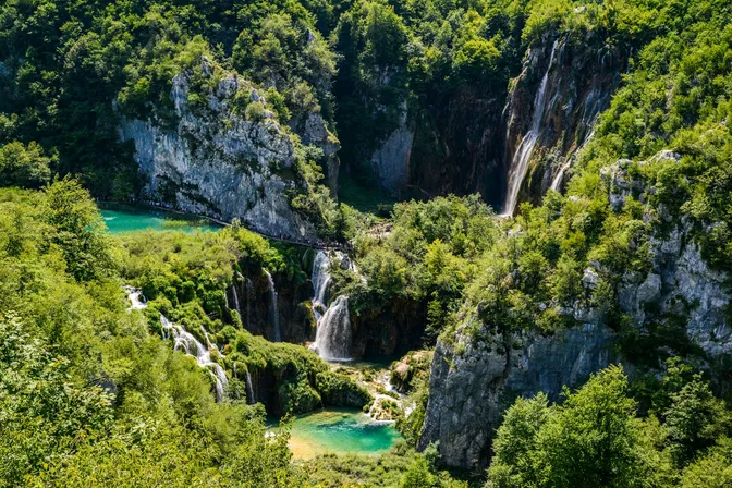 Plitvice's Lower Lakes from above: turquoise pools and cascades in a forested limestone canyon, with the tall Veliki slap waterfall on the right