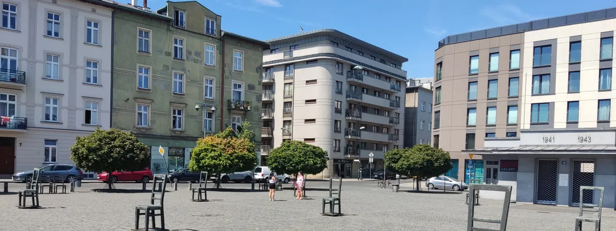 Bronze empty chairs of the Ghetto Heroes Square memorial in Podgórze, Kraków, with the wartime "1941"/"1943" building markings visible behind them
