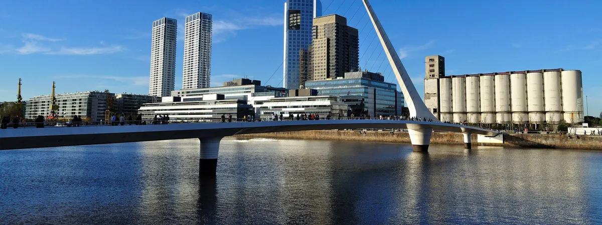 The white cable-stayed Puente de la Mujer footbridge in Puerto Madero, with the neighborhood's glass towers and converted dock warehouses behind it