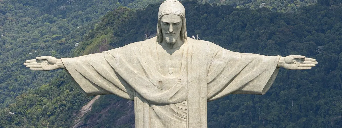 The outstretched arms of the Christ the Redeemer statue atop Corcovado mountain, seen close up against the forested hillside