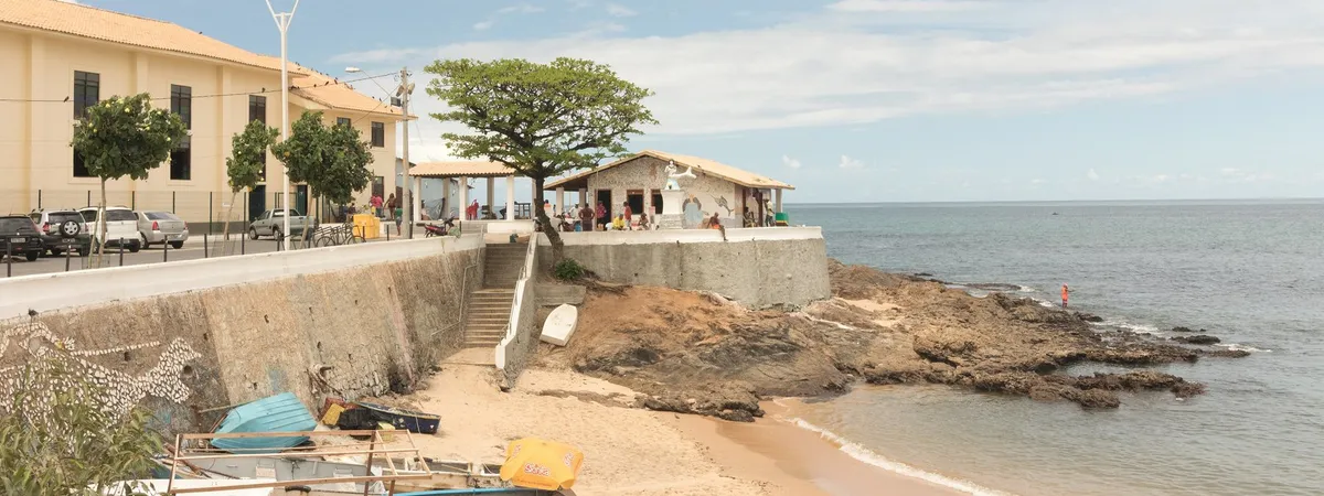 El pequeño santuario encalado de Casa de Iemanjá sobre un promontorio rocoso frente al mar en Rio Vermelho, con barcas de pesca varadas en la playa cercana
