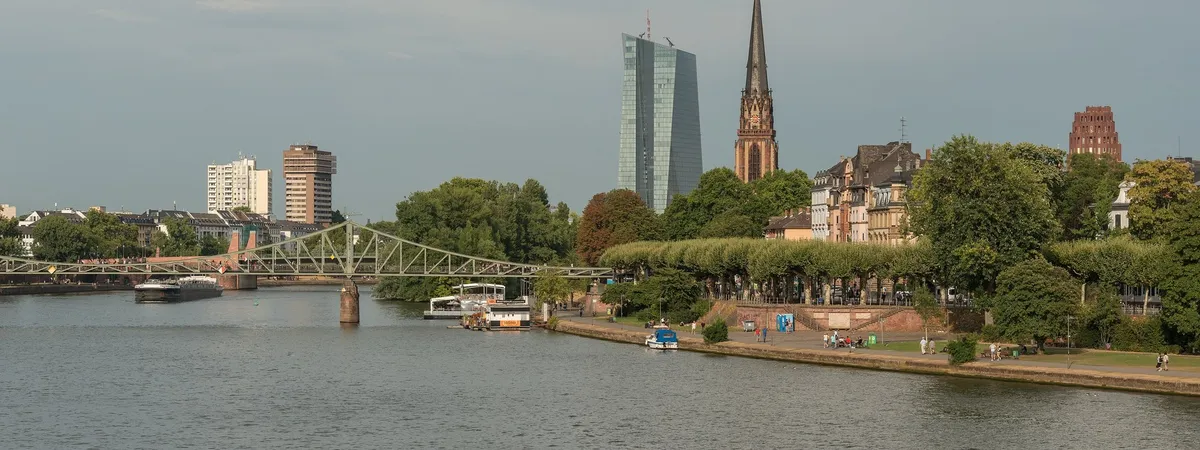 The Museumsufer riverside promenade in Sachsenhausen, with the Eiserner Steg footbridge, the Dreikönigskirche's spire, and the European Central Bank tower across the Main