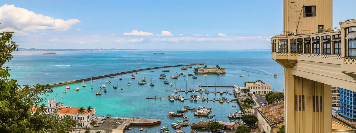 The Elevador Lacerda rising above Salvador's harbor, with fishing boats anchored in the turquoise water of the Baía de Todos os Santos