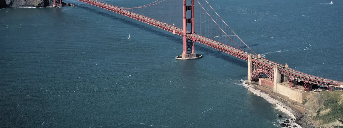 Aerial view of the Golden Gate Bridge spanning the strait between the Marin Headlands and San Francisco, with sailboats on the water below