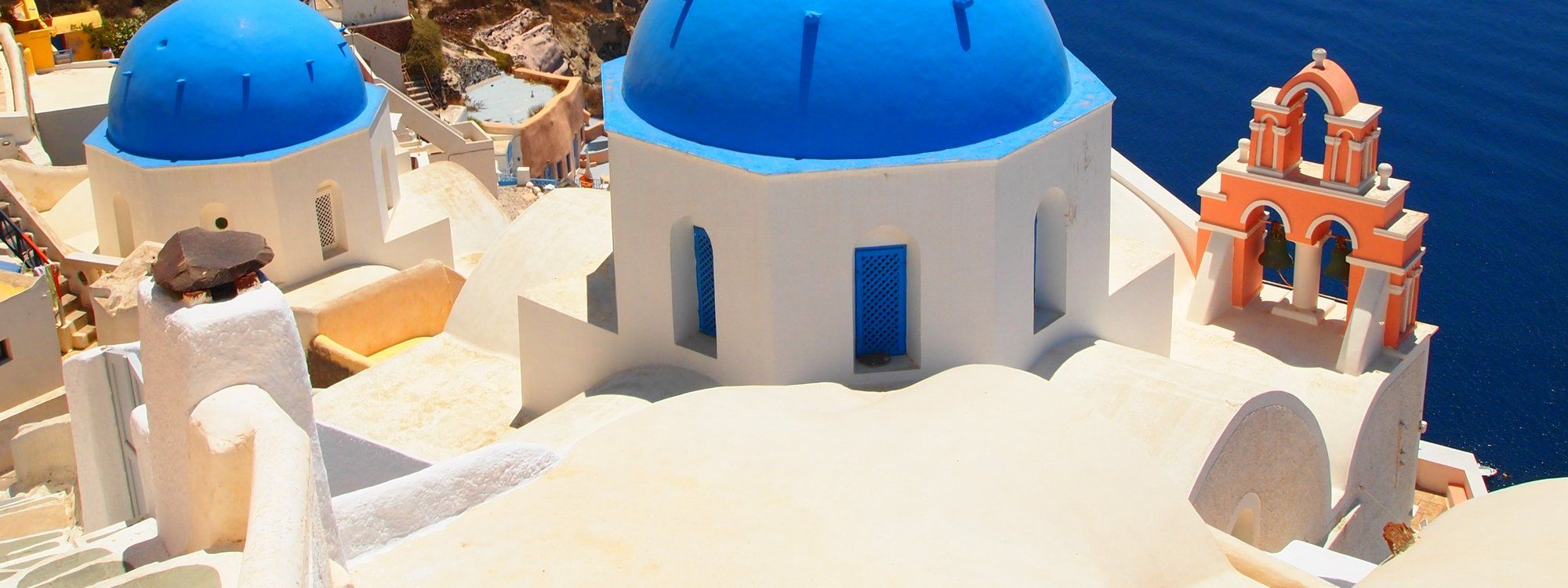 Blue-domed churches and a coral bell tower overlooking the caldera in Oia, Santorini