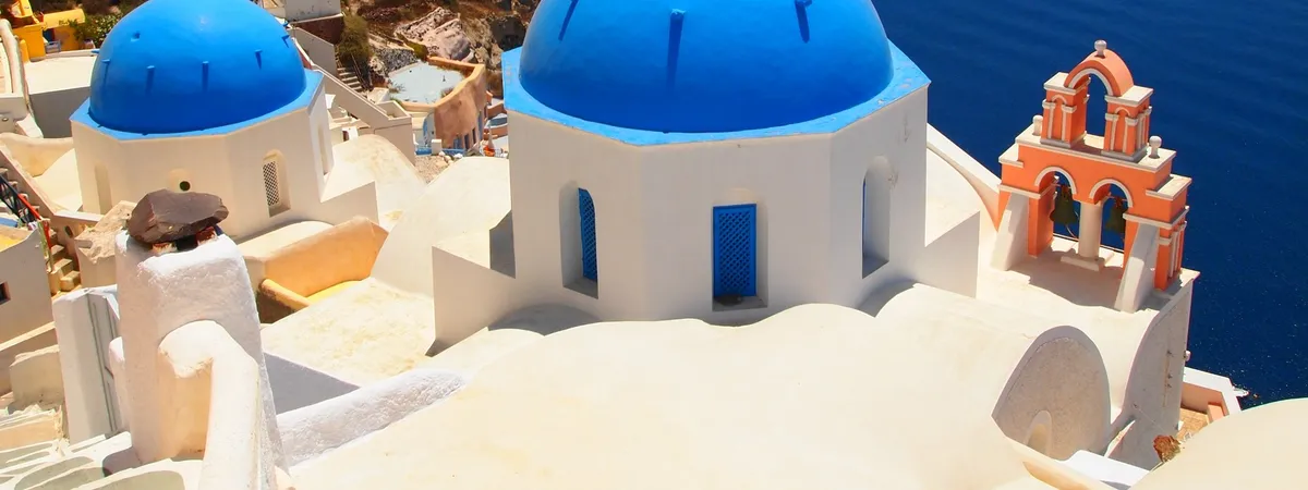 Blue-domed churches and a coral bell tower overlooking the caldera in Oia, Santorini